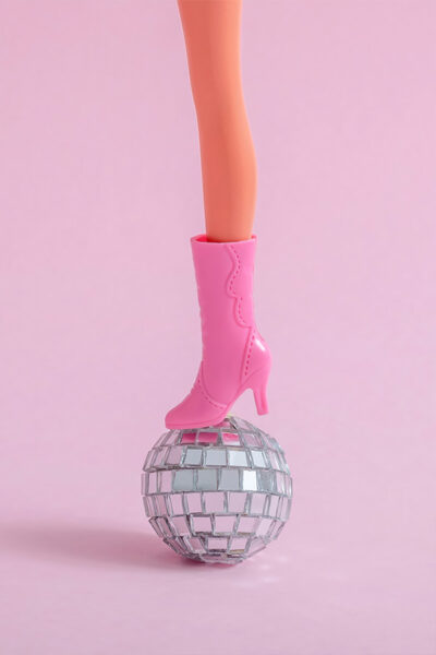 Doll feet on a small disco ball on a pink wall